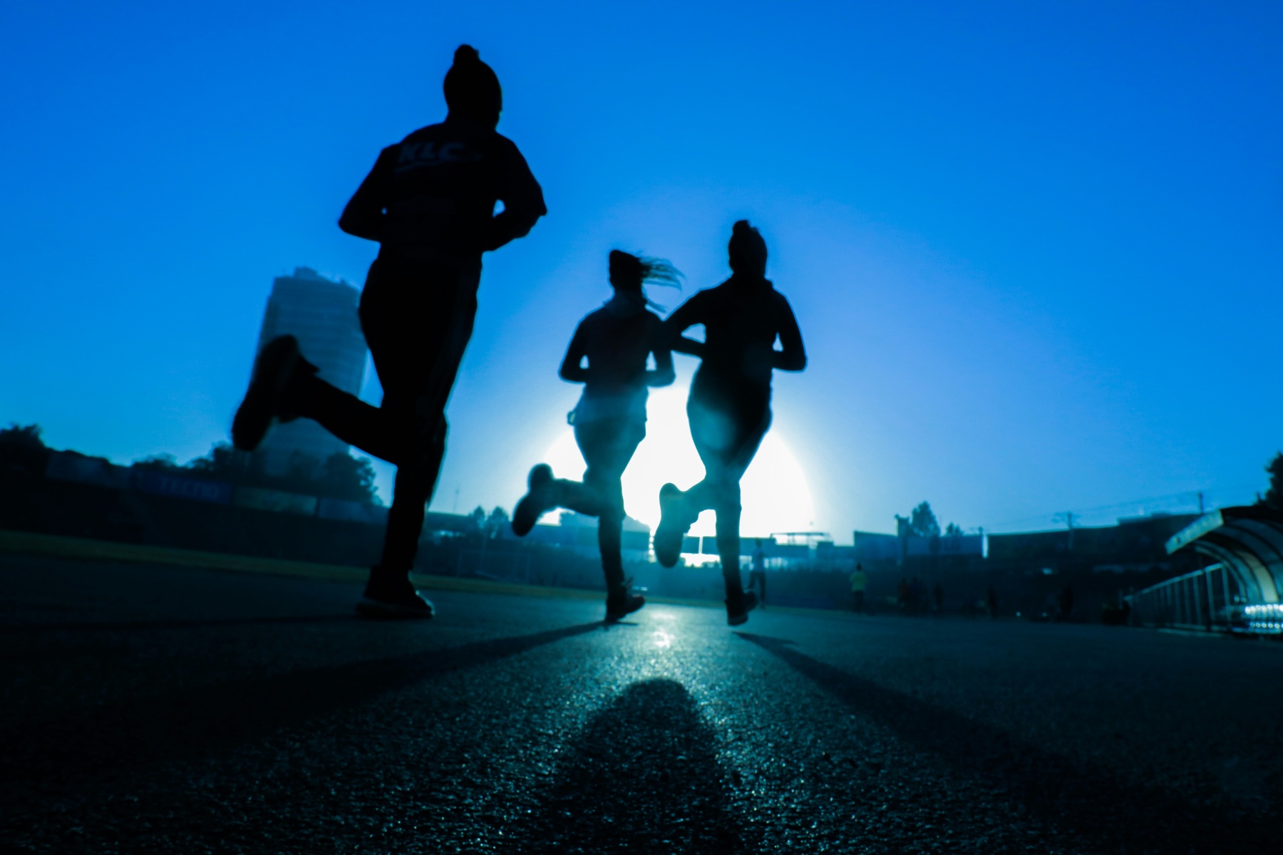 Three runners training together on a track at sunrise