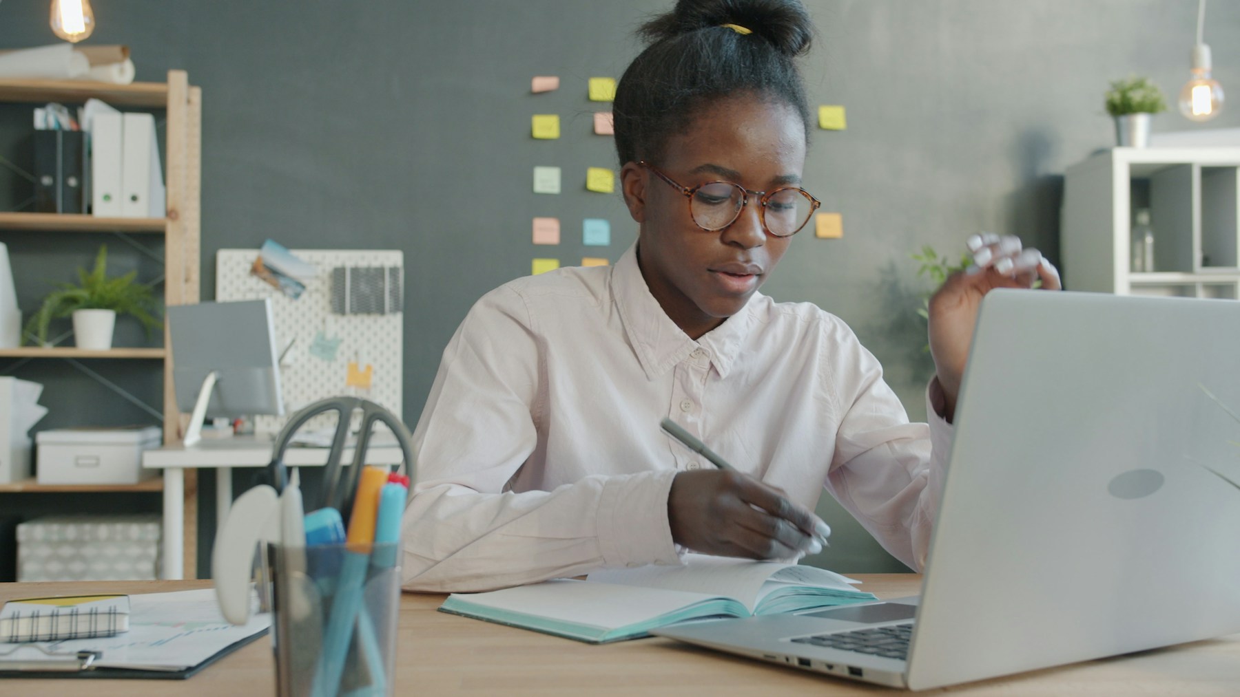 A Black woman tracking her progress in a notebook while working at her laptop